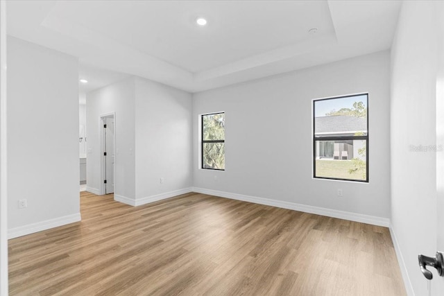 empty room with recessed lighting, light wood-style flooring, baseboards, and a tray ceiling