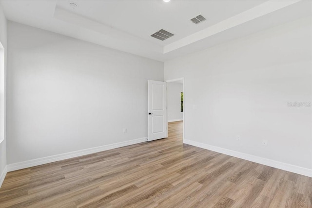 unfurnished room featuring visible vents, light wood-style flooring, a raised ceiling, and baseboards