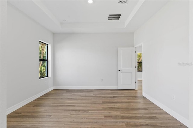 empty room featuring wood finished floors, visible vents, baseboards, recessed lighting, and a raised ceiling