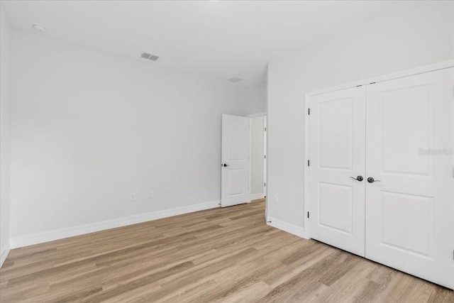 unfurnished bedroom with a closet, baseboards, visible vents, and light wood-style flooring