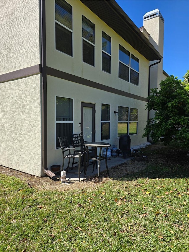 back of property with stucco siding, a chimney, a lawn, and a patio