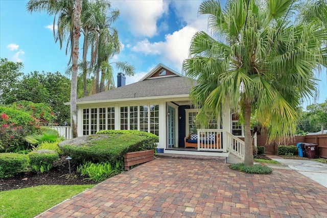 doorway to property featuring fence, covered porch, and a chimney