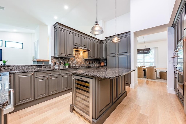 kitchen with dark stone counters, wine cooler, backsplash, and light wood-style flooring