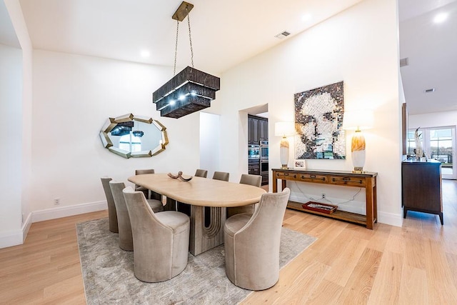 dining space with visible vents, baseboards, a towering ceiling, and light wood finished floors