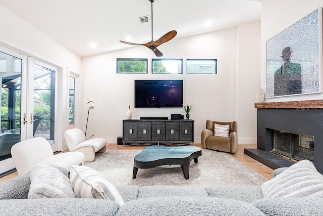 living room featuring visible vents, a fireplace with raised hearth, a ceiling fan, wood finished floors, and lofted ceiling