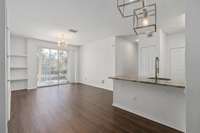 unfurnished living room with an inviting chandelier, baseboards, a sink, dark wood-style floors, and visible vents