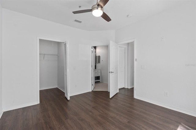 unfurnished bedroom with a walk in closet, baseboards, dark wood finished floors, visible vents, and a closet