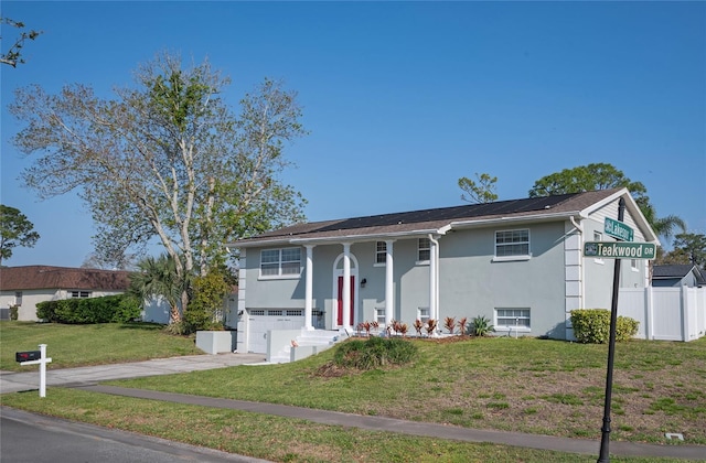 view of front of home featuring a front yard, fence, driveway, an attached garage, and roof mounted solar panels