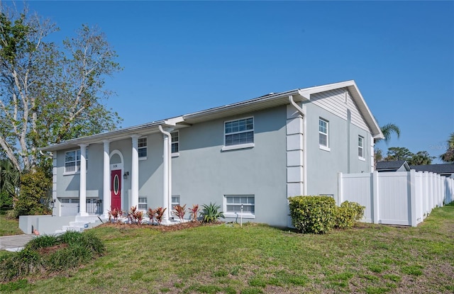 bi-level home featuring stucco siding, a front yard, and fence