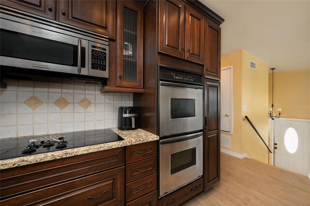 kitchen featuring light wood-type flooring, decorative backsplash, stainless steel appliances, dark brown cabinetry, and glass insert cabinets