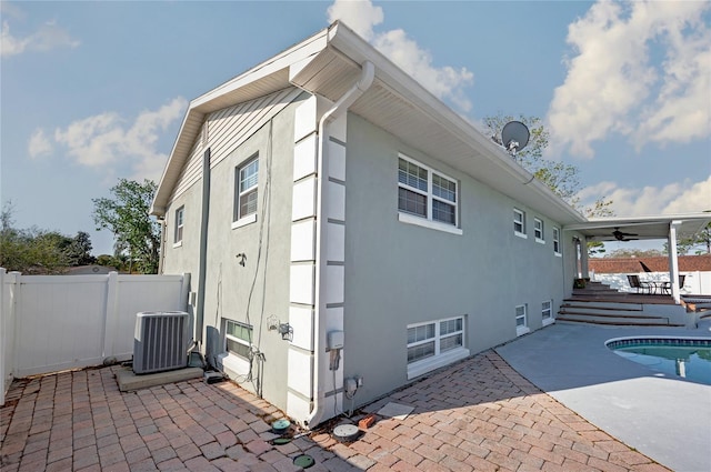 view of side of property featuring a patio area, fence, central AC, and stucco siding