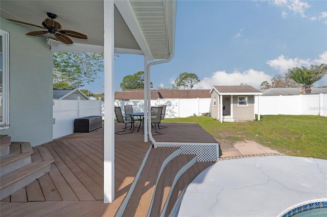 wooden deck featuring outdoor dining space, a ceiling fan, a fenced backyard, an outdoor structure, and a lawn