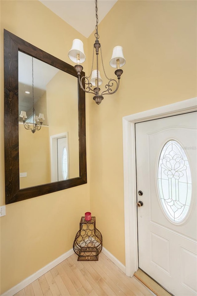 foyer featuring vaulted ceiling, baseboards, an inviting chandelier, and wood finished floors