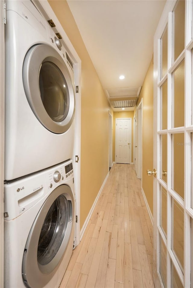 washroom featuring baseboards, light wood-style floors, stacked washer and clothes dryer, and laundry area