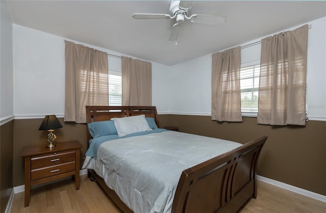 bedroom featuring ceiling fan, baseboards, multiple windows, and light wood-style flooring