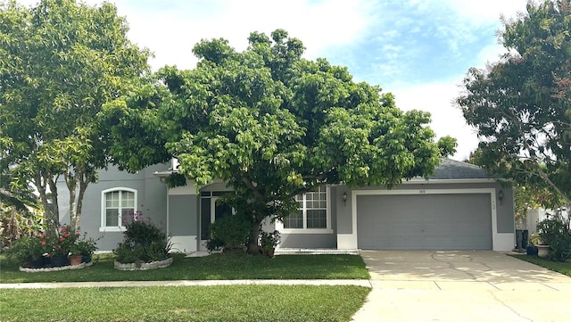 view of property hidden behind natural elements with roof with shingles, driveway, an attached garage, stucco siding, and a front lawn