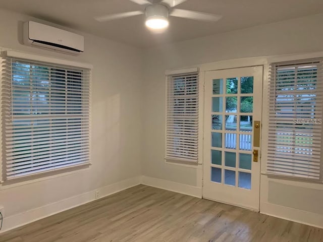 unfurnished room with a wall mounted air conditioner, baseboards, wood finished floors, and a ceiling fan