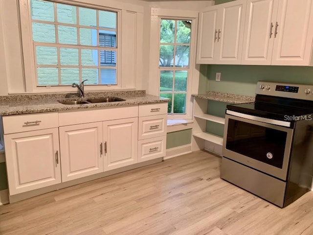 kitchen with stainless steel electric stove, light stone counters, light wood-style flooring, white cabinetry, and a sink