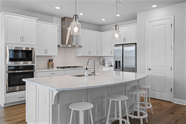 kitchen with visible vents, a sink, stainless steel appliances, white cabinets, and wall chimney range hood