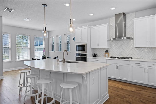 kitchen featuring visible vents, a sink, appliances with stainless steel finishes, white cabinetry, and wall chimney exhaust hood