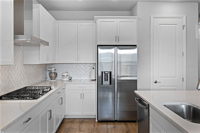 kitchen with a sink, white cabinets, appliances with stainless steel finishes, wall chimney range hood, and backsplash