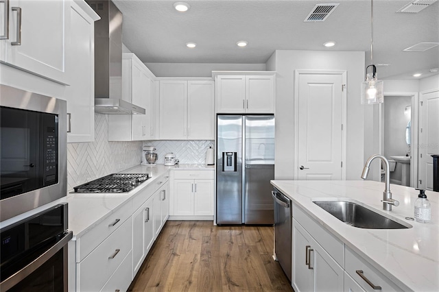 kitchen with visible vents, white cabinets, stainless steel appliances, wall chimney exhaust hood, and a sink