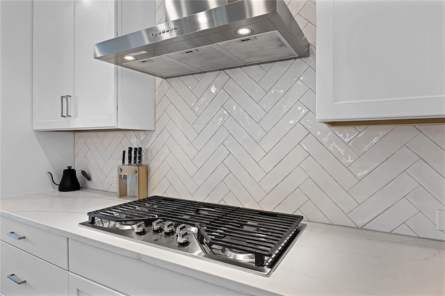 kitchen featuring light stone counters, stainless steel gas cooktop, decorative backsplash, white cabinets, and wall chimney exhaust hood