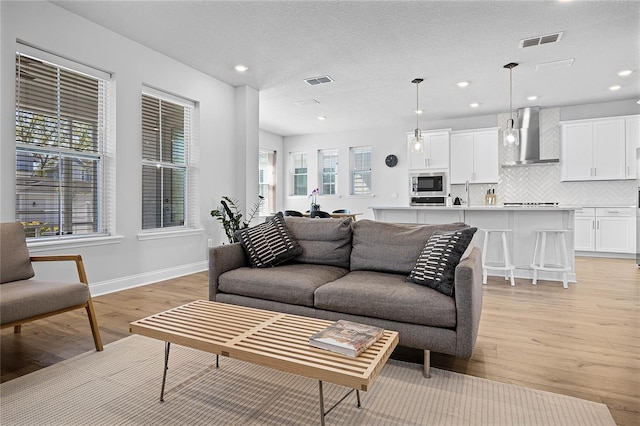 living area with recessed lighting, visible vents, baseboards, and light wood finished floors