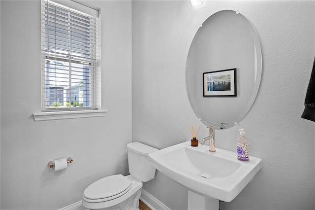 half bathroom with toilet, baseboards, and a sink