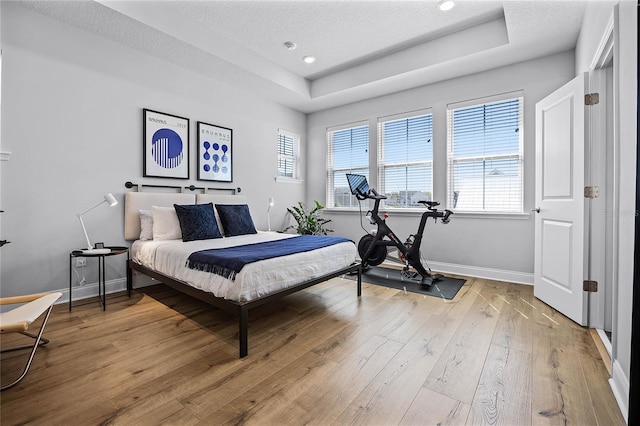 bedroom with baseboards, recessed lighting, light wood-style floors, a textured ceiling, and a raised ceiling