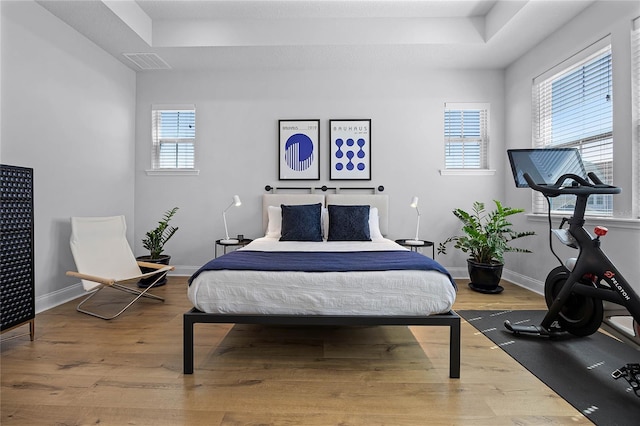 bedroom featuring visible vents, a raised ceiling, baseboards, and wood finished floors