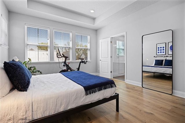 bedroom featuring baseboards, a tray ceiling, light wood-style floors, a textured ceiling, and connected bathroom