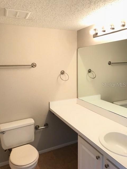 bathroom featuring tile patterned floors, visible vents, toilet, a textured ceiling, and vanity