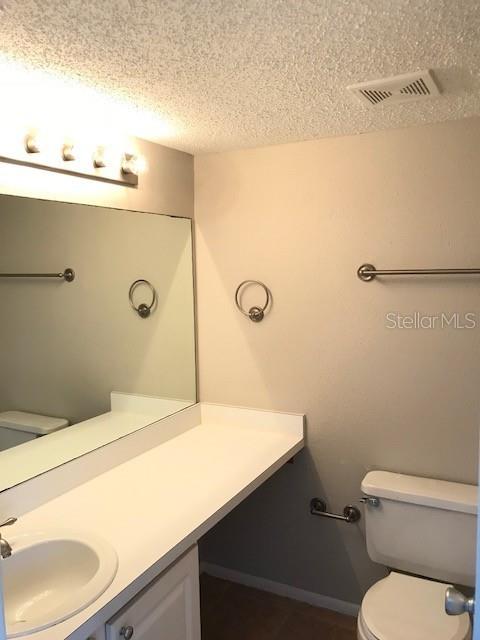 bathroom featuring visible vents, toilet, vanity, and a textured ceiling