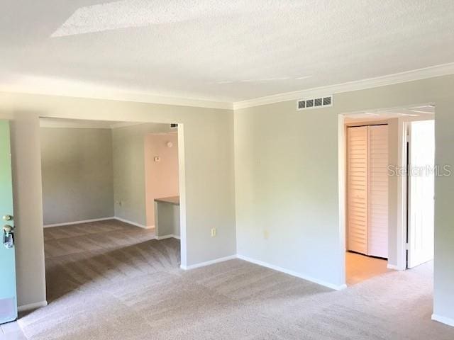 carpeted spare room with visible vents, a textured ceiling, crown molding, and baseboards