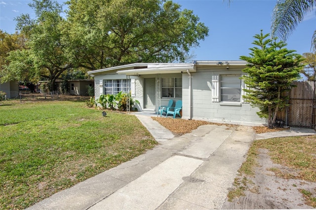 view of front facade featuring concrete block siding, a front yard, and fence