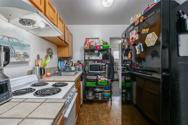 kitchen featuring white range with electric cooktop, under cabinet range hood, stainless steel microwave, freestanding refrigerator, and brown cabinetry