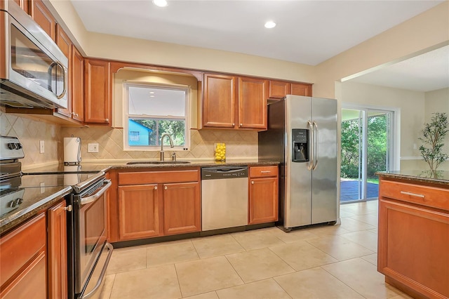 kitchen with a sink, stainless steel appliances, brown cabinetry, and dark stone countertops