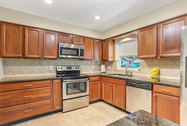 kitchen featuring a sink, appliances with stainless steel finishes, dark stone countertops, and light tile patterned floors