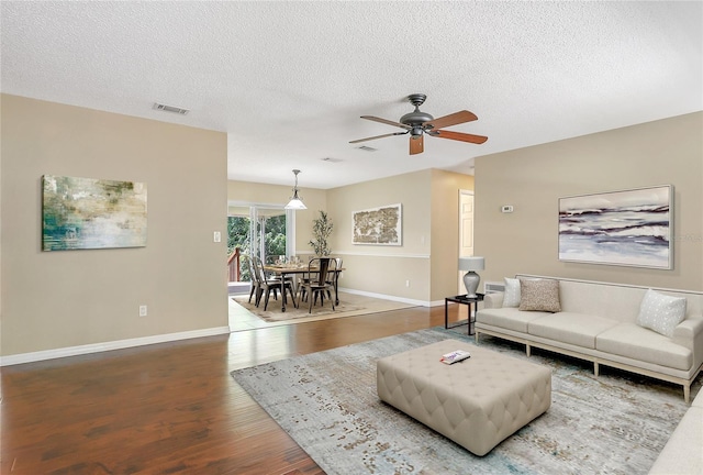 living room featuring visible vents, baseboards, wood finished floors, and a ceiling fan