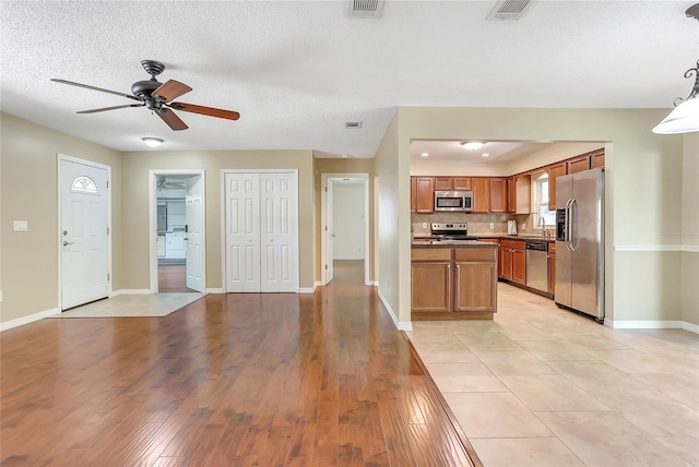 kitchen featuring a ceiling fan, visible vents, appliances with stainless steel finishes, brown cabinets, and backsplash