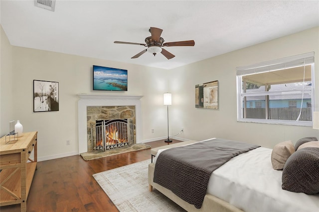 bedroom with visible vents, baseboards, a fireplace, wood finished floors, and a ceiling fan