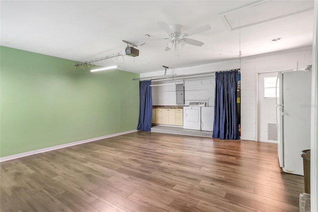 unfurnished room featuring baseboards, attic access, wood finished floors, a ceiling fan, and separate washer and dryer