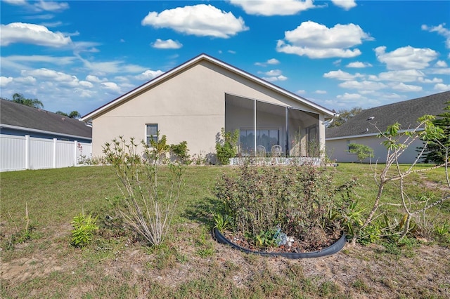 rear view of property with a yard, fence, a sunroom, and stucco siding