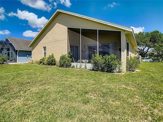 back of property featuring stucco siding, a lawn, and a sunroom