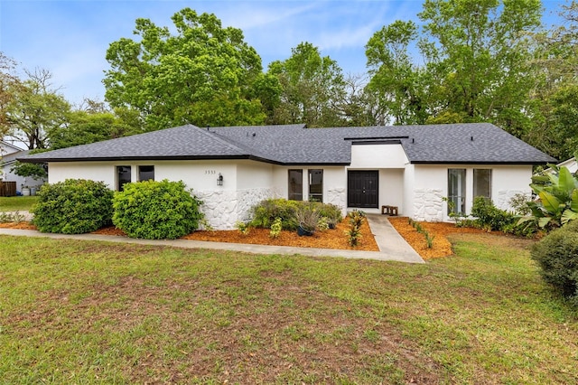 view of front of house with stucco siding, a front yard, and roof with shingles