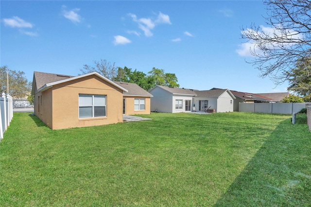 back of house featuring stucco siding, a yard, and fence