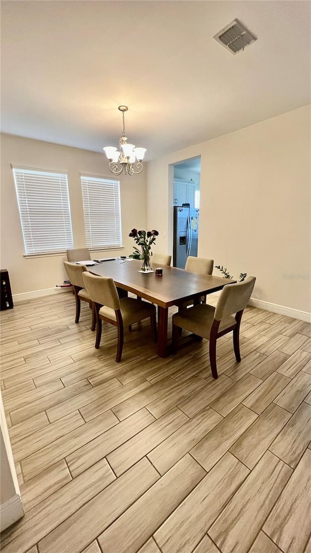 dining space featuring visible vents, baseboards, an inviting chandelier, and light wood-style flooring