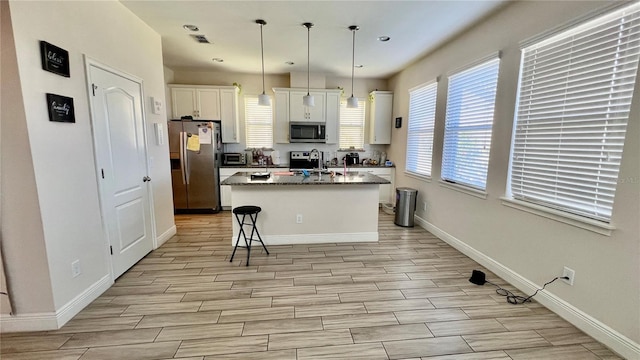 kitchen with baseboards, wood finish floors, a center island with sink, stainless steel appliances, and white cabinetry