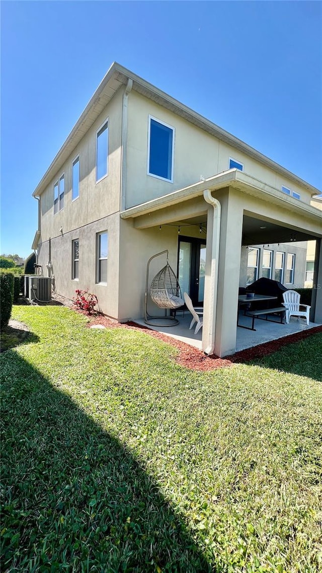 rear view of house with central air condition unit, a patio area, a lawn, and stucco siding